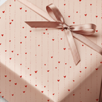 Romantic light pink wrapping paper with red heart pattern and a delicate satin ribbon bow, perfect for Valentine's Day or anniversary gifts.