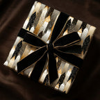 Elegant gift wrapped in modern black, gold, and white wrapping paper with a black velvet bow.