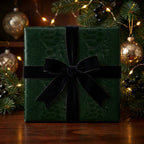 Dark green Christmas gift wrap with black velvet ribbon, festive ornaments and tree boughs. Wrapped Studios.