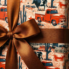 Rustic western wrapping paper with red vintage trucks and a brown satin bow by Wrapped Studios.