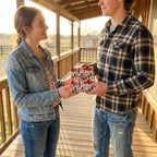 Rustic western wrapping paper with red vintage trucks on a gift held by a couple. Wrapped Studios.