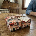 Vintage western wrapping paper with red retro trucks and cacti on a rustic gift box from Wrapped Studios.
