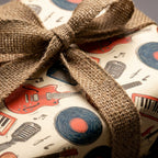 Retro music gift wrap with guitars and vinyl records, tied with a burlap bow by Wrapped Studios.