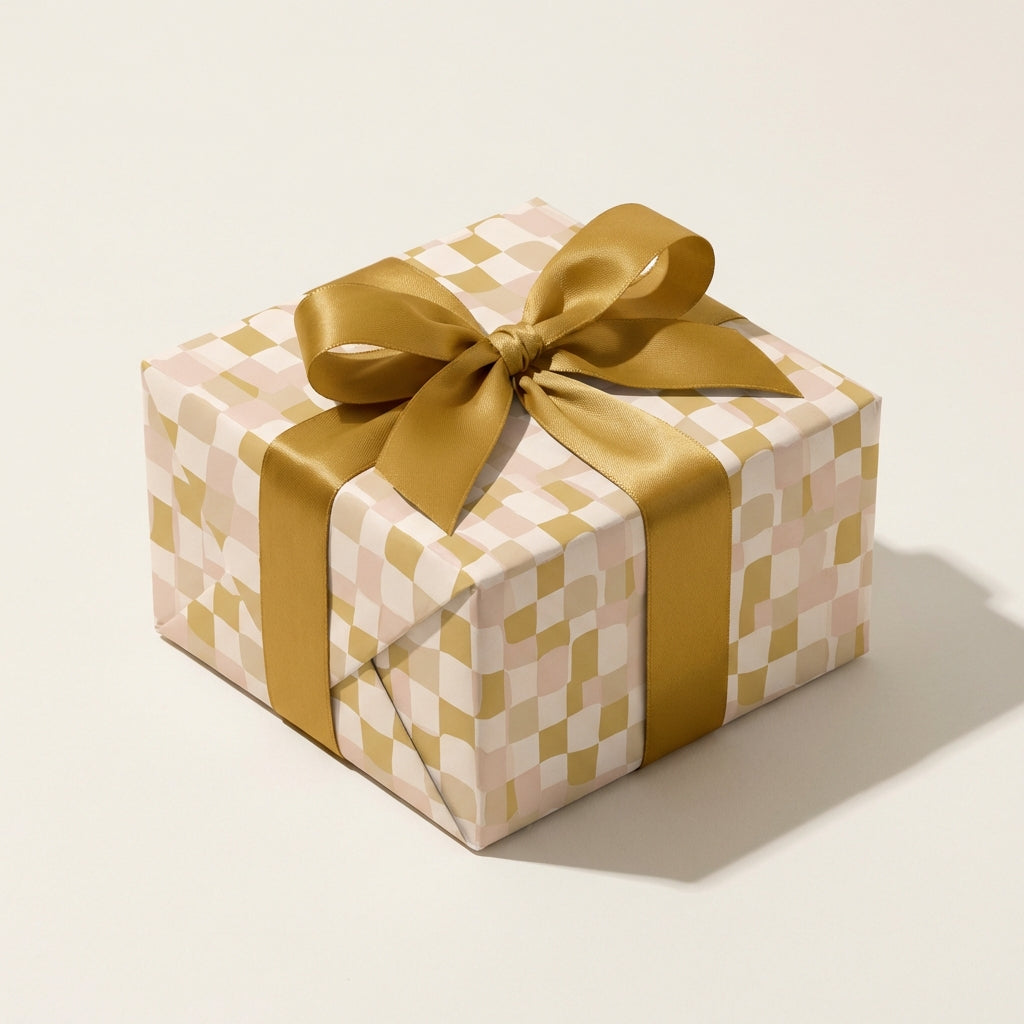 Modern wavy checkerboard gift wrap in gold, blush pink, and cream tones, tied with a luxurious gold satin ribbon bow.
