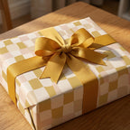 Aesthetic checkerboard wrapping paper in warm yellow and beige tones on a gift box tied with a large mustard yellow ribbon.