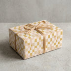 Modern wavy checkered wrapping paper in earth tones of mustard and pink, tied with a natural raffia bow.