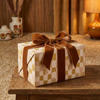 Gift wrapped in retro wavy checkerboard paper with earth tones and a luxurious brown velvet bow on a rustic wooden table.