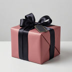 Elegant gift wrapping: Solid blush wrapping paper with black satin ribbon bow and blank tag.