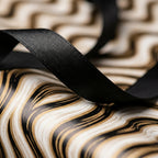 Elegant black and gold wavy wrapping paper with a black ribbon, luxury gift wrap by Wrapped Studios.