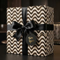 Modern black and gold wavy wrapping paper on a luxury gift box with satin bow by Wrapped Studios.