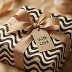 Luxury gift wrap with modern black and cream wavy pattern, gold ribbon, and gift tag by Wrapped Studios.