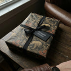 Rustic woodland wrapping paper with bear and leaf design, tied with a black ribbon.