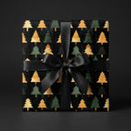 Elegant Christmas gift wrapped in black paper with gold and green trees and a black ribbon bow.