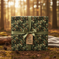Rustic gift wrapped in botanical print wrapping paper with green ribbon and a tag that reads, "From Our Forest to Yours."