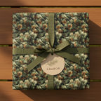 Square gift box wrapped in green pine branch Christmas wrapping paper with an olive green ribbon and tag.