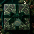 Luxury Christmas wrapping paper with pine pattern, green velvet bow, and holiday tag by Wrapped Studios.