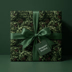 Luxury Christmas gift wrap with green pine branch pattern, satin bow, and Wrapped Studios tag.