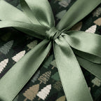 Forest green Christmas wrapping paper with pine tree pattern and sage satin bow by Wrapped Studios.