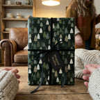 Green Christmas wrapping paper with a pine tree pattern and black ribbon by Wrapped Studios.