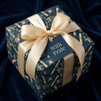 Navy and gold graduation wrapping paper with mortarboards and a cream satin ribbon bow by Wrapped Studios.