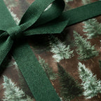 Rustic Christmas gift wrap with watercolor pine trees and green ribbon by Wrapped Studios.