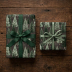 Rustic pine tree Christmas wrapping paper on gifts with green ribbons on wood, by Wrapped Studios.