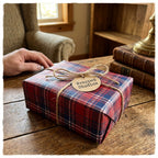 Red plaid Christmas wrapping paper by Wrapped Studios on a rustic gift box tied with twine on a wooden table.