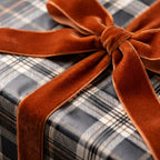 Plaid wrapping paper in black and grey with a luxury burnt orange velvet bow by Wrapped Studios.