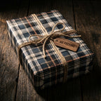 Rustic plaid Christmas wrapping paper with twine and a wood gift tag on a dark wooden table by Wrapped Studios.