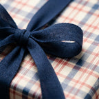 Rustic plaid wrapping paper in navy and red with a textured blue bow, perfect holiday gift wrap by Wrapped Studios.