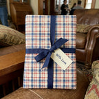 Cozy blue and red plaid wrapping paper with a navy blue ribbon and gift tag, from Wrapped Studios.