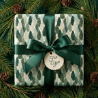 Elegant forest tree Christmas gift wrap with green satin bow and pine branches by Wrapped Studios.