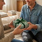 Cozy couple exchanging a gift with green botanical holiday wrapping paper and velvet ribbon, by Wrapped Studios.