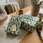 Rustic botanical holiday wrapping paper with green pine leaf pattern on cozy gifts by Wrapped Studios.
