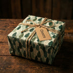 Rustic green forest holiday wrapping paper with a twine bow and Cheers tag on a gift box by Wrapped Studios.