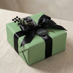 Sage green gift box with a black ribbon and floral decoration on a beige surface