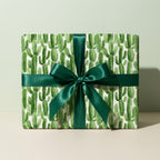 Modern cactus wrapping paper with an emerald green satin bow on a gift box by Wrapped Studios.