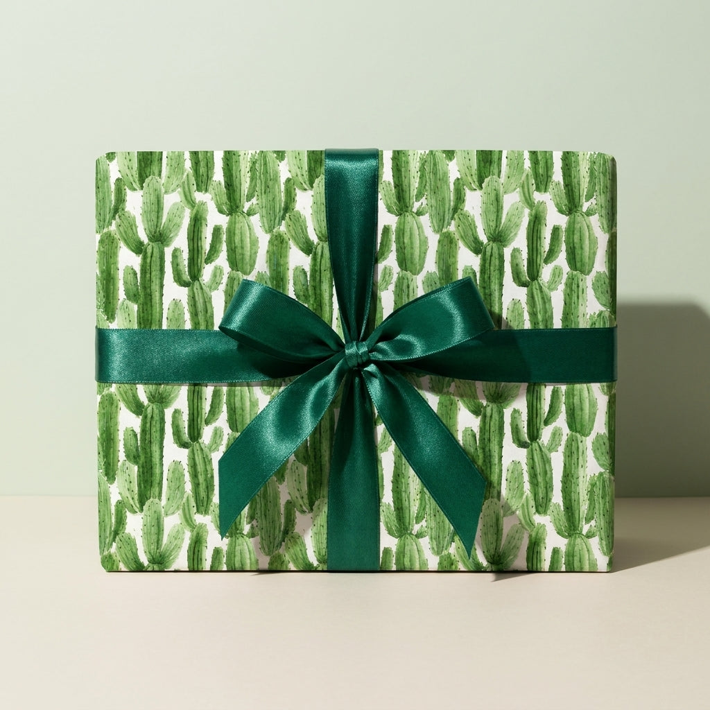 Modern cactus wrapping paper with an emerald green satin bow on a gift box by Wrapped Studios.