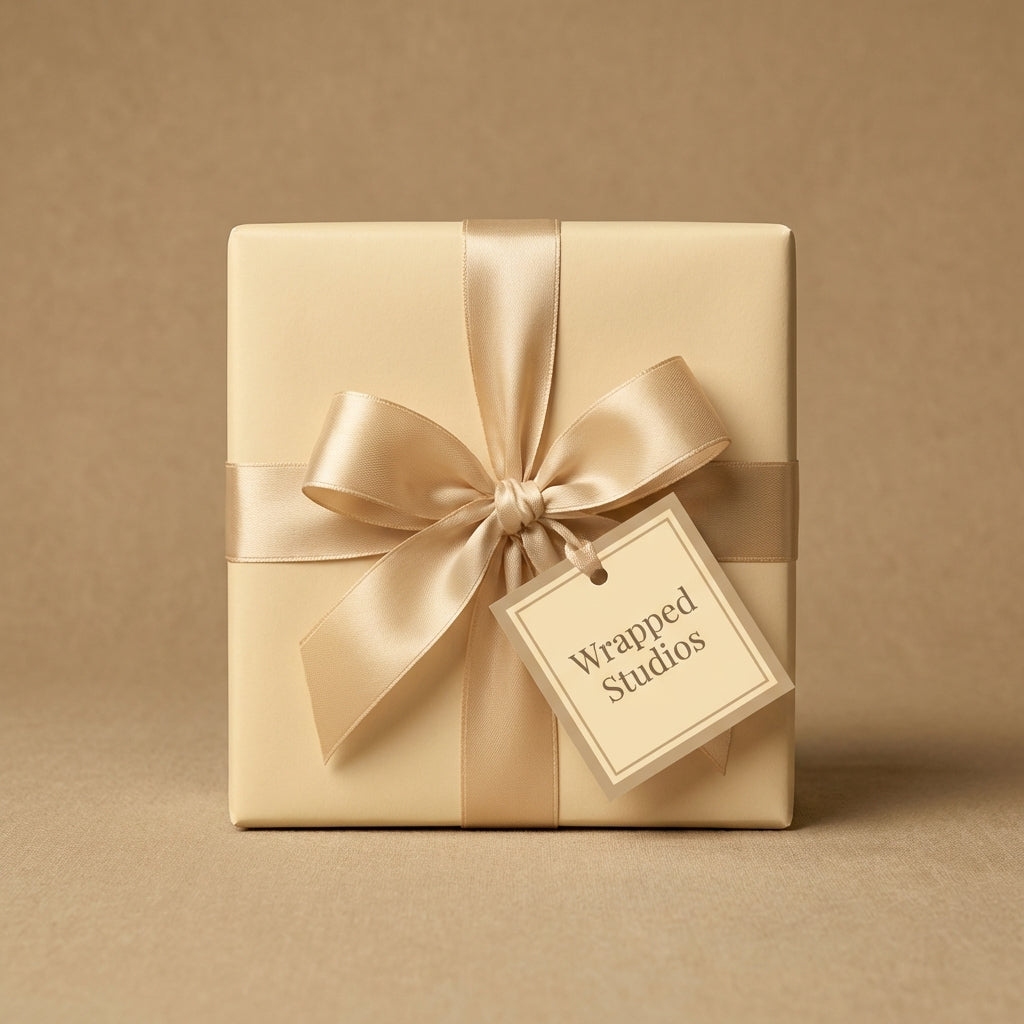 Elegant square gift wrapped in solid beige paper with a gold satin bow and matching tag.