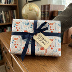 Chemistry wrapping paper with beakers and molecules, tied with a navy ribbon by Wrapped Studios.