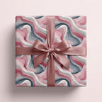 Square gift wrapped in pink, grey, and white abstract watercolor paper with rose gold satin ribbon.