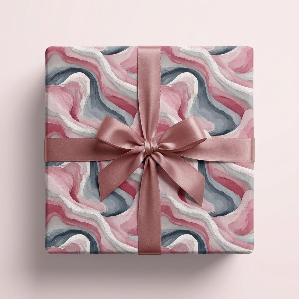 Square gift wrapped in pink, grey, and white abstract watercolor paper with rose gold satin ribbon.