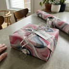 Square gift in pink and grey watercolor wrapping paper with silver ribbon and "Celebrate" tag.