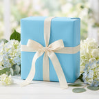 Light blue gift wrapped in solid color wrapping paper with cream ribbon, elegant present for birthday or wedding.