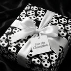 Soccer ball wrapping paper with a white satin bow and champion gift tag by Wrapped Studios.