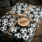 Black and white soccer wrapping paper by Wrapped Studios on a gift tied with a twine bow and wood tag.