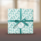 Square gift wrapped in teal balloon-patterned wrapping paper with teal ribbon and tag.