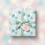 Pastel balloon print wrapping paper on a square gift box, tied with a light green satin bow and a tag.