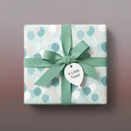 Wrapped gift with light blue balloon wrapping paper, green ribbon, and "A Little Treat!" tag.