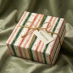Striped holiday wrapping paper in green and coral with gold dots, tied with gold string and a tag that says "With Love."